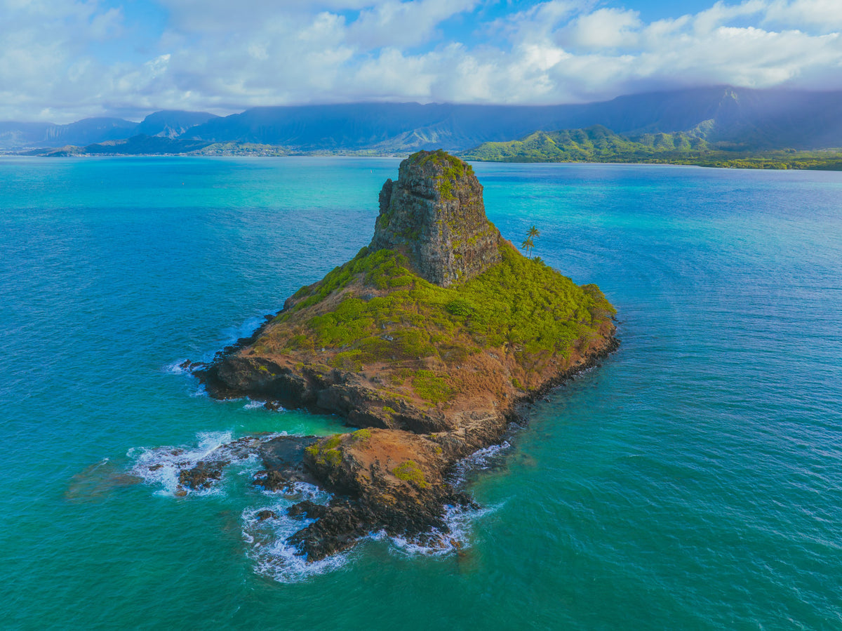 Aerial photo of Mokolii Island in turquoise water with the Koolau mountains, Oahu