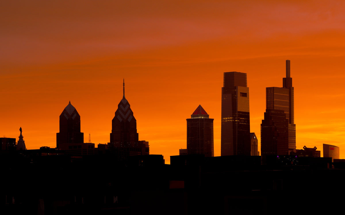 Philadelphia skyline silhouetted against an orange sunset sky