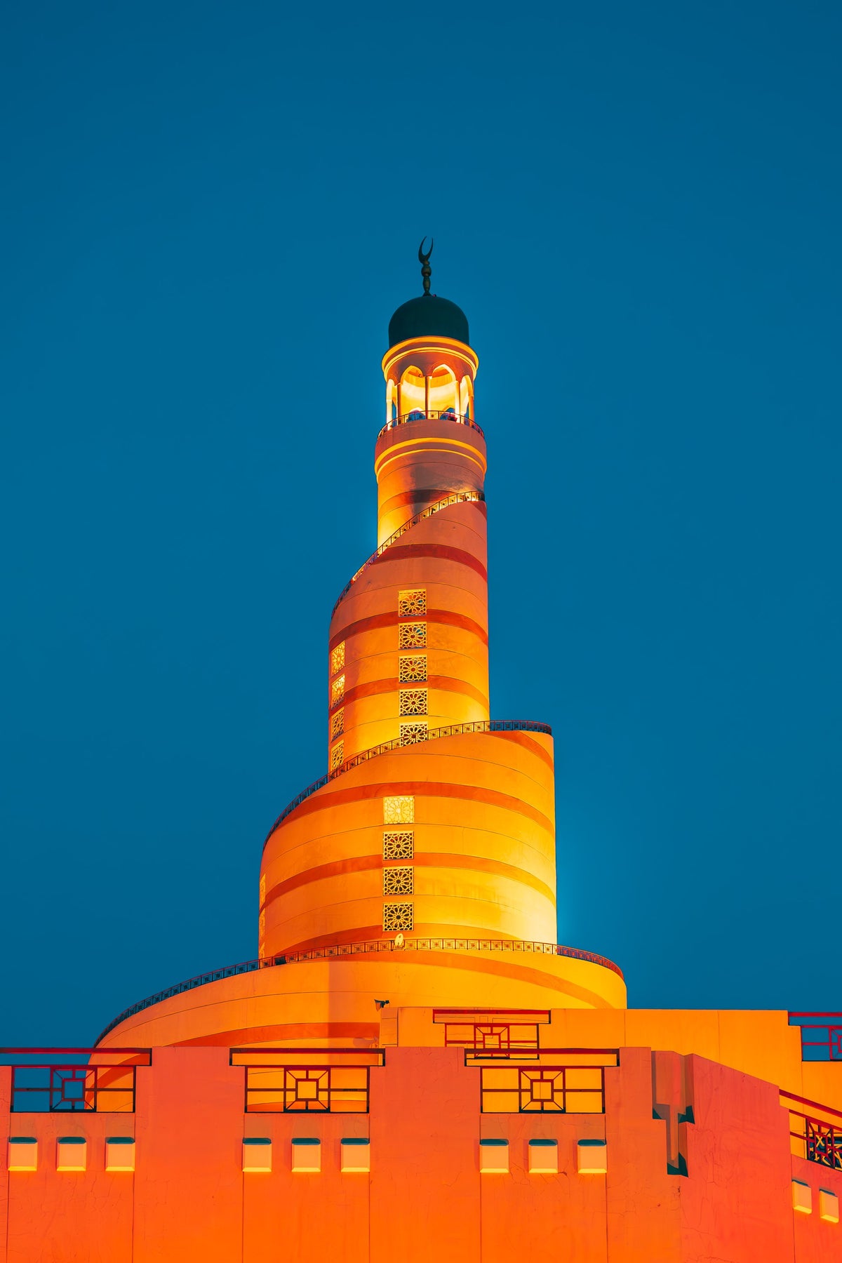 The spiral minaret of the Fanar lit orange against a blue evening sky in Doha