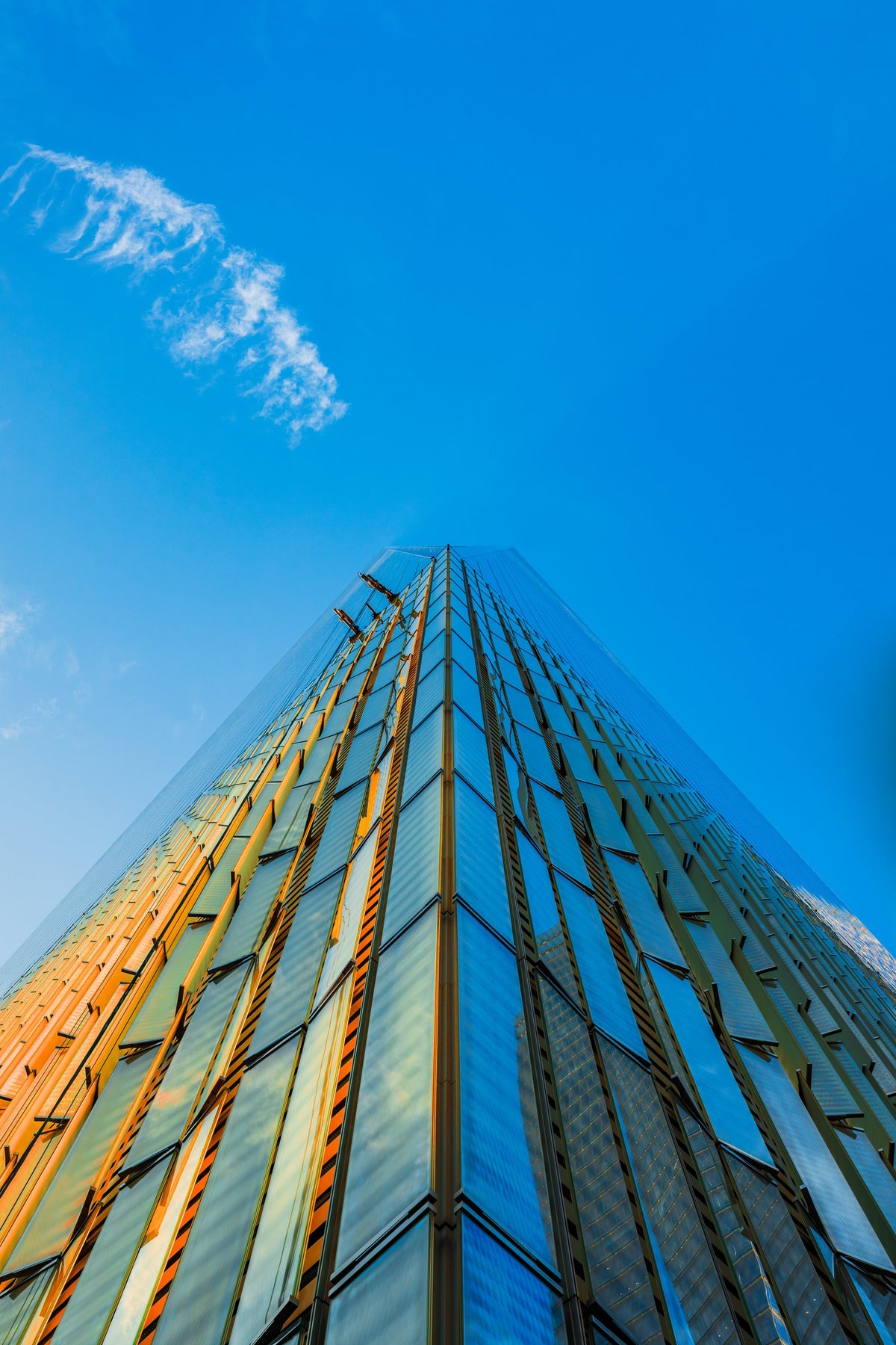 A glass skyscraper facade shot from its base into blue sky