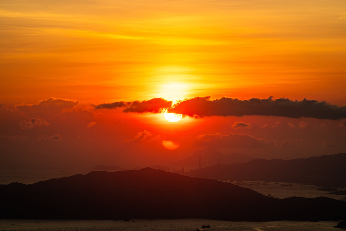 A red sun setting behind dark hills and clouds in Hong Kong