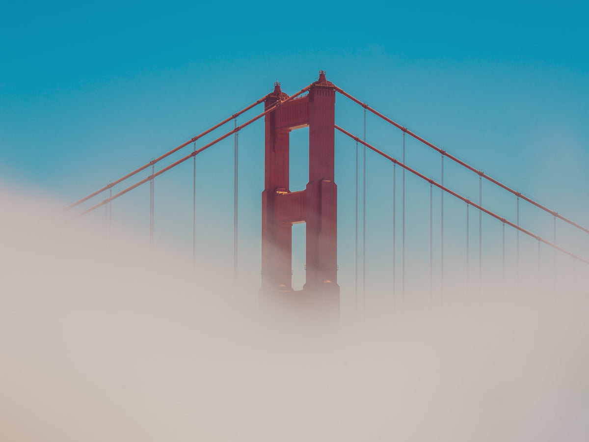 Golden Gate Bridge tower rising above the fog against a blue sky, San Francisco