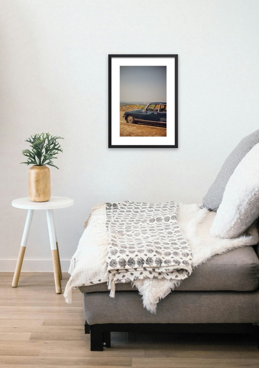 Black-framed print shown on a wall: A vintage sedan parked on a dusty hilltop in Portugal