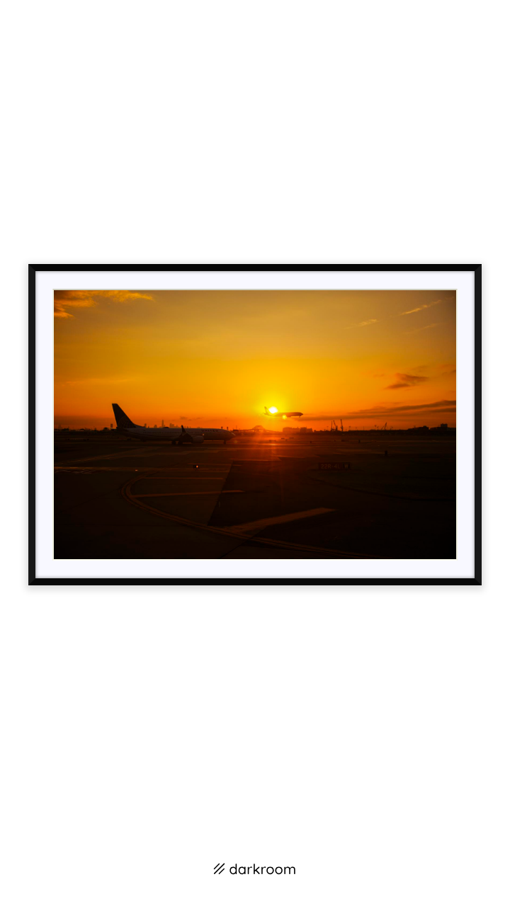 Black-framed print: A plane in silhouette on the runway as the sun sets
