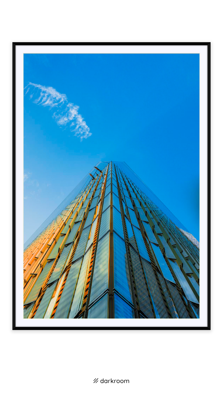 Black-framed print: A glass skyscraper facade shot from its base into blue sky