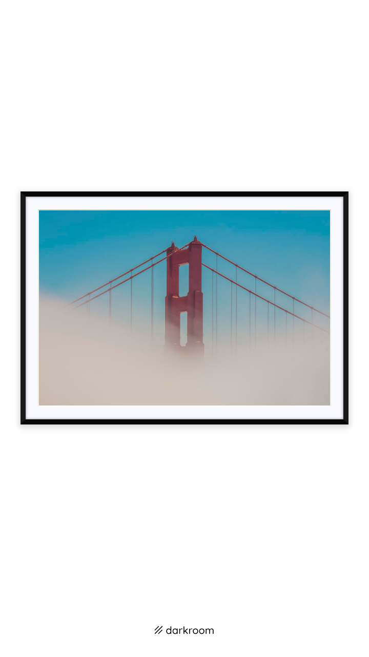 Black-framed print: Golden Gate Bridge tower rising above the fog against a blue sky, San Francisco