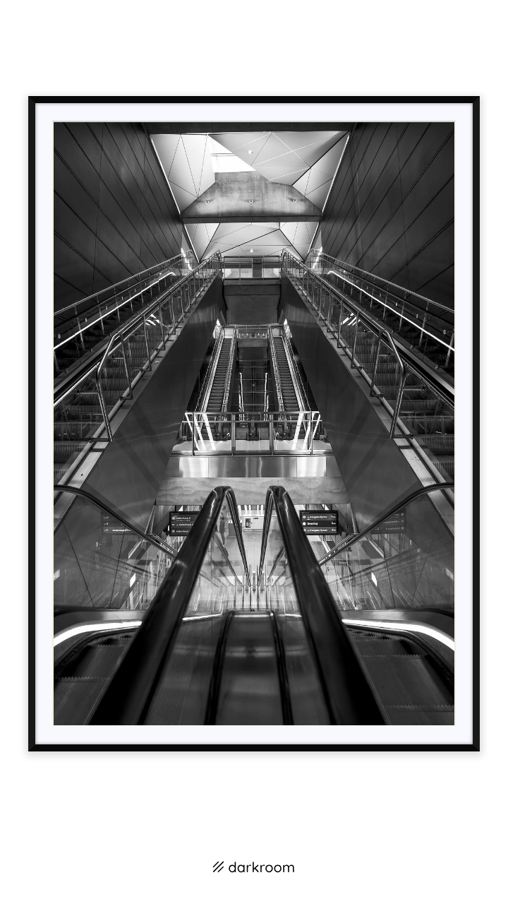 Black-framed print: Black and white escalators and angled ceiling panels in symmetry