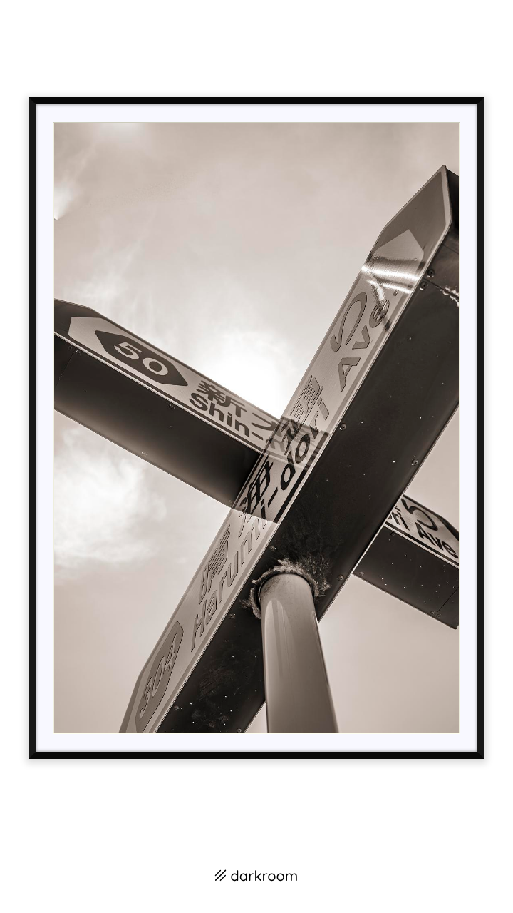 Black-framed print: Two street signs crossing against a sepia sky