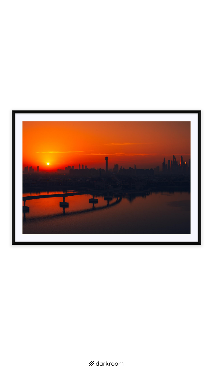 Black-framed print: The sun rising beside the Dubai skyline over gold and red water
