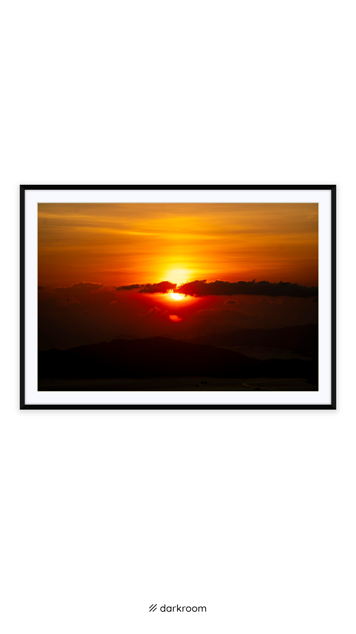 Black-framed print: A red sun setting behind dark hills and clouds in Hong Kong