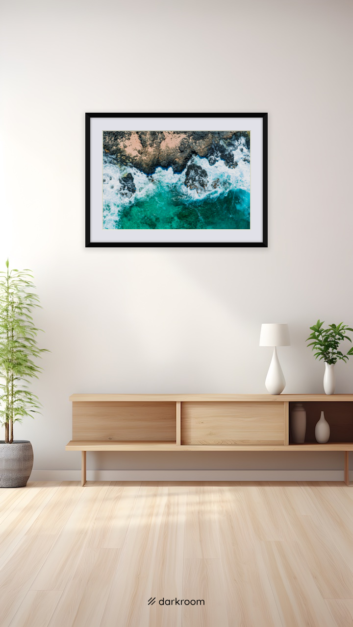 Black-framed print shown on a wall: Aerial photo of foam and lava rock on the Oahu coast, Hawaii